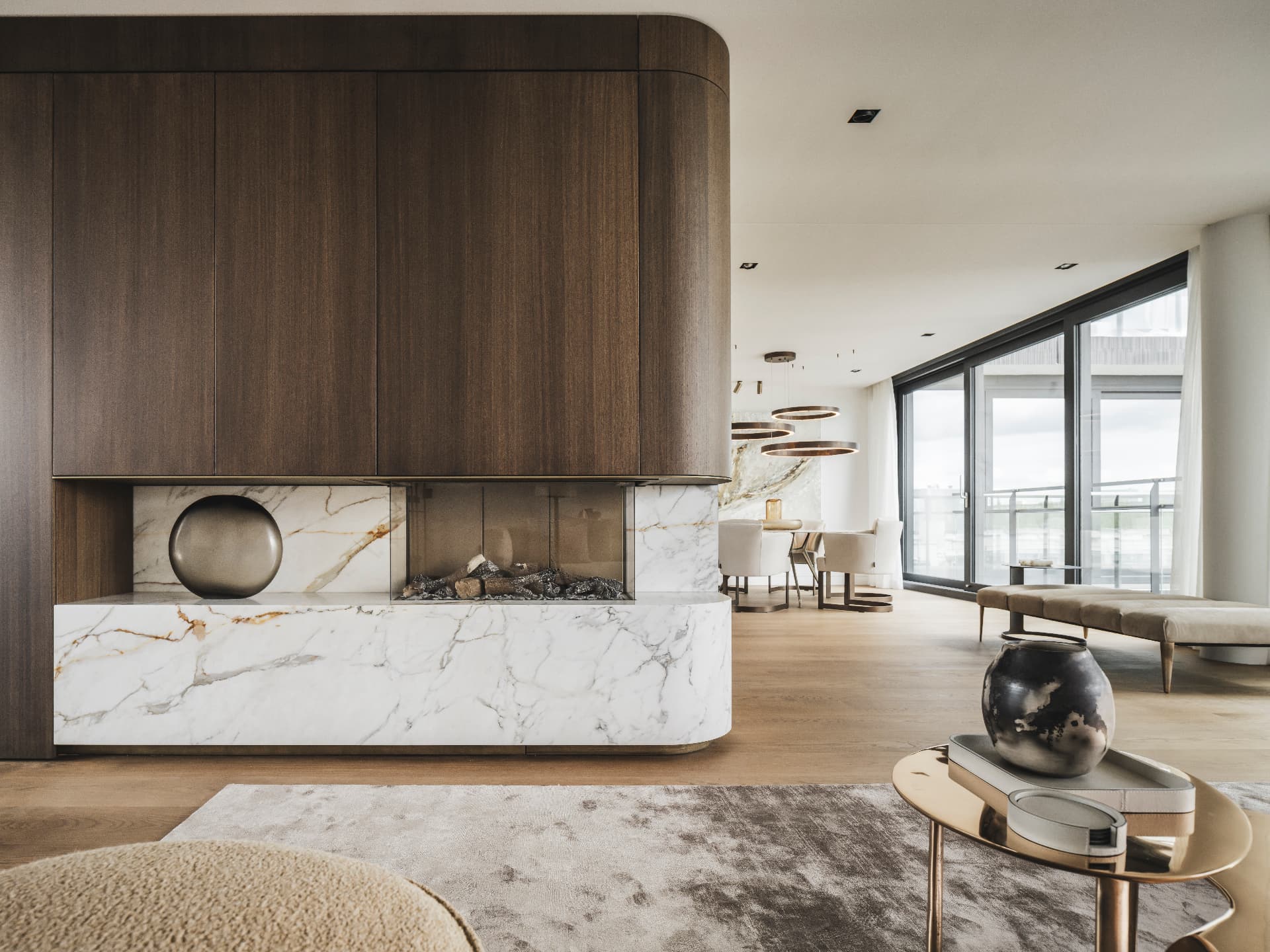 Contemporary living space with a marble fireplace and dark wood panelling by House of Culimaat